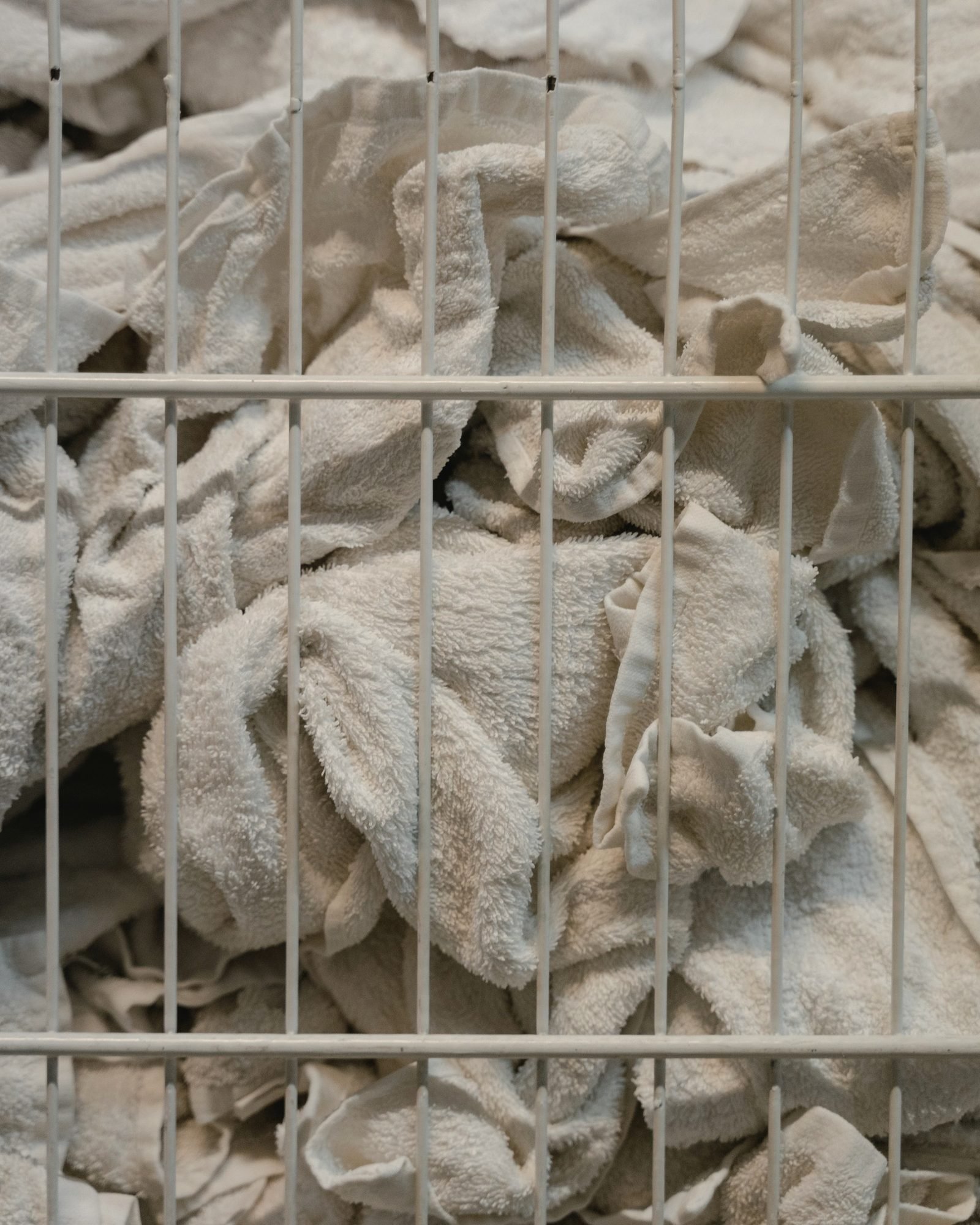 White towels behind the wire grid of a laundry cart